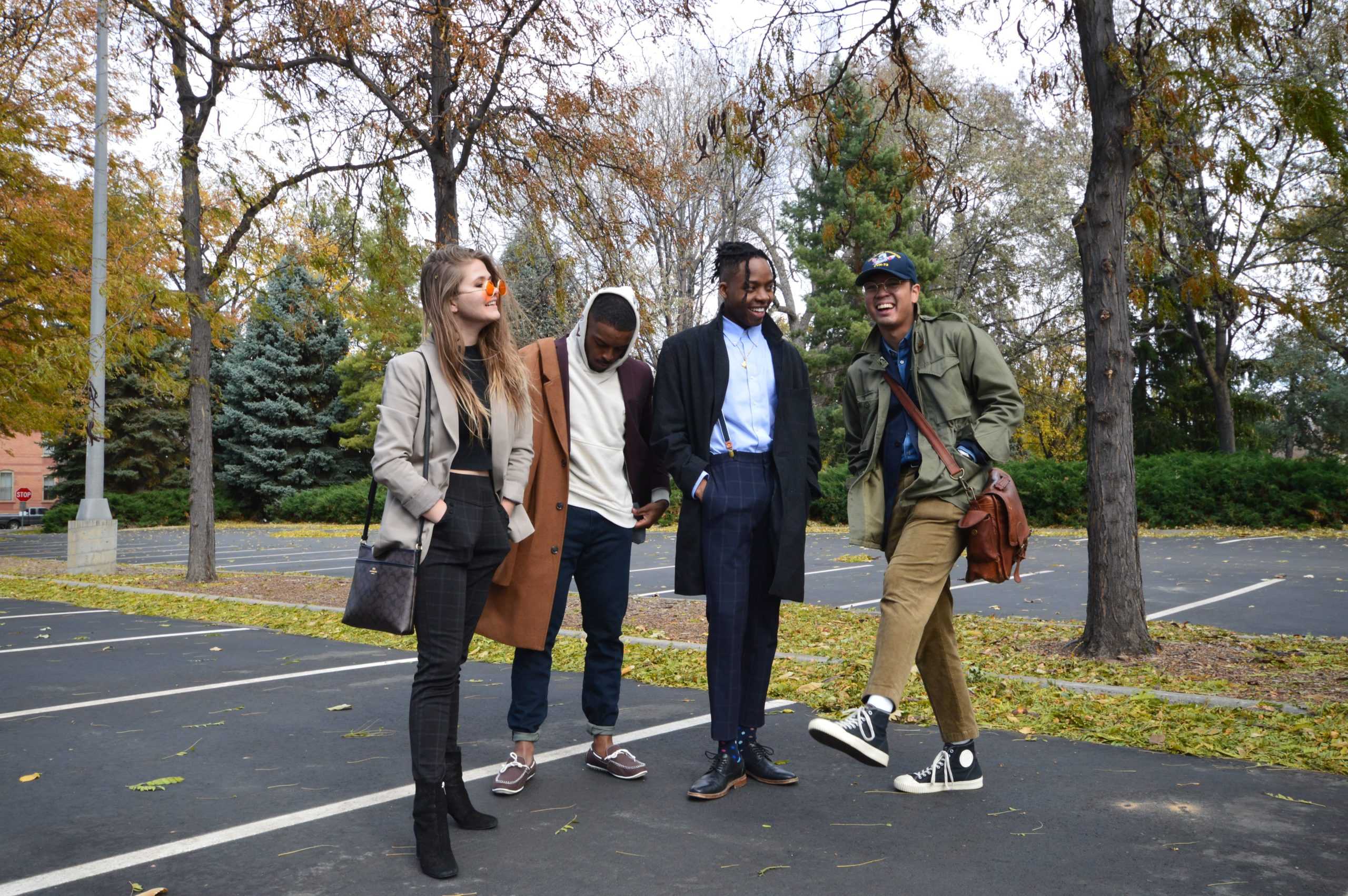 Four people, one white woman, two black men, and one Filipino man, stand in a parking lot dressed in fashionable Ivy style