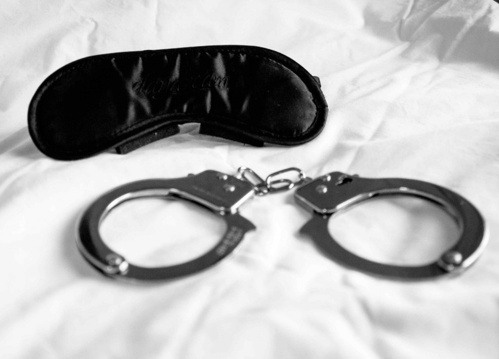 Handcuffs and sleeping mask on a bed.