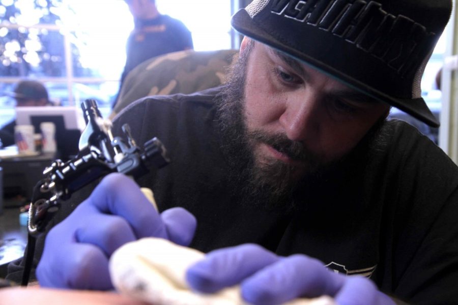 Rob Nicholl carefully tattoos an atom symbol on Vera Bendonis side at Covenant Tattoo shop.