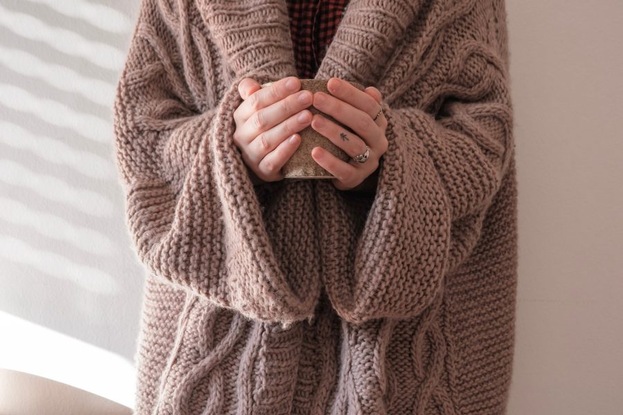 white person in a chunky cardigan holding a mug