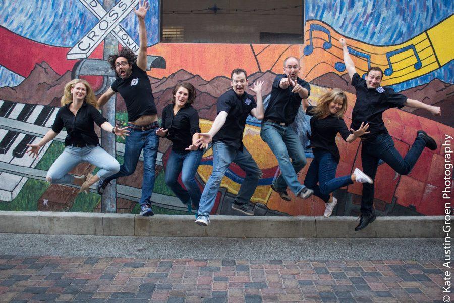 Members of the Comedy Brewers jumping up in smiles in front of Old Town mural