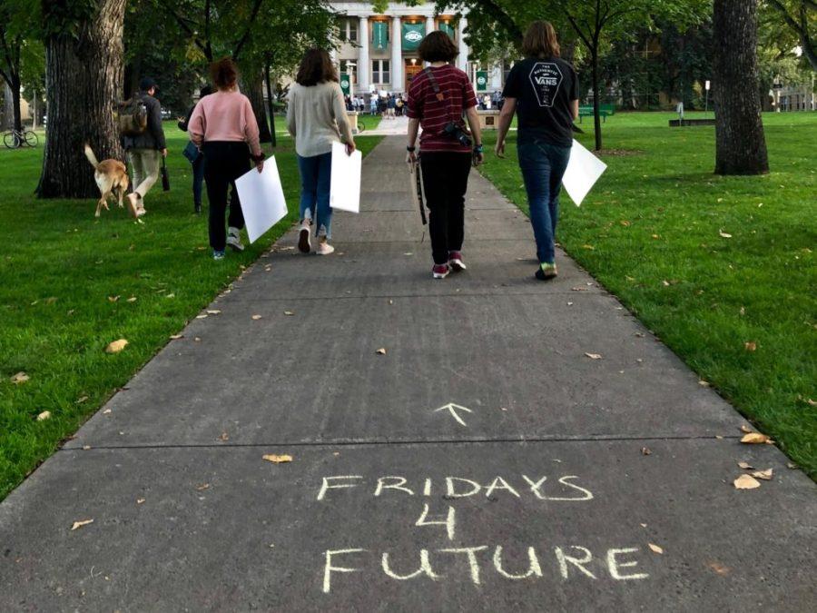 four students holding protest signs walking toward the CSU admin building. Sidewalk chalk on ground reads Fridays 4 Future
