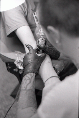 person tattooing another persons arm. Black and white photo.
