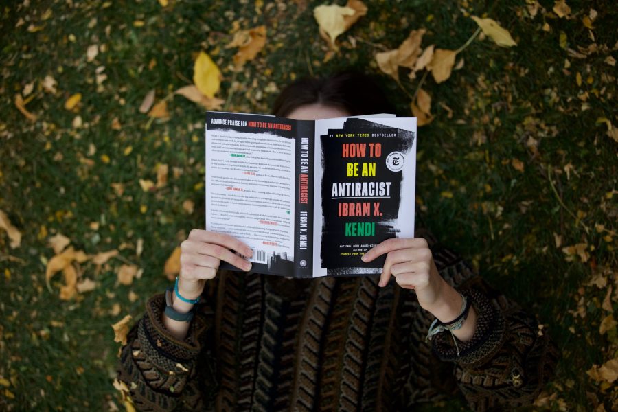Student holding up the book How to be an Antiracist by Ibram X. Kendi over their face