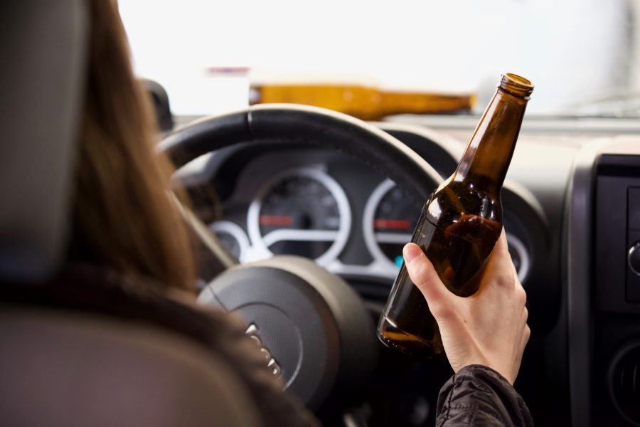 Person in driver's seat of car holding a bottle of alcohol