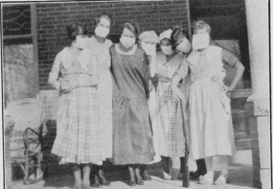 historical photo of women wearing masks standing arms around each other