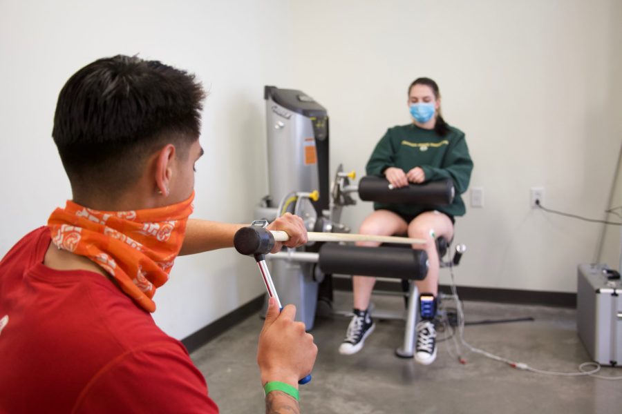 Maximilliano Martinez and Brooke Elges demonstrate an activity to study the stretch reflex for a health and exercise science lab on Mar. 9. This activity was modified, using a six-foot poll to adhere to social distancing requirements (Ryan Schmidt | College Avenue).