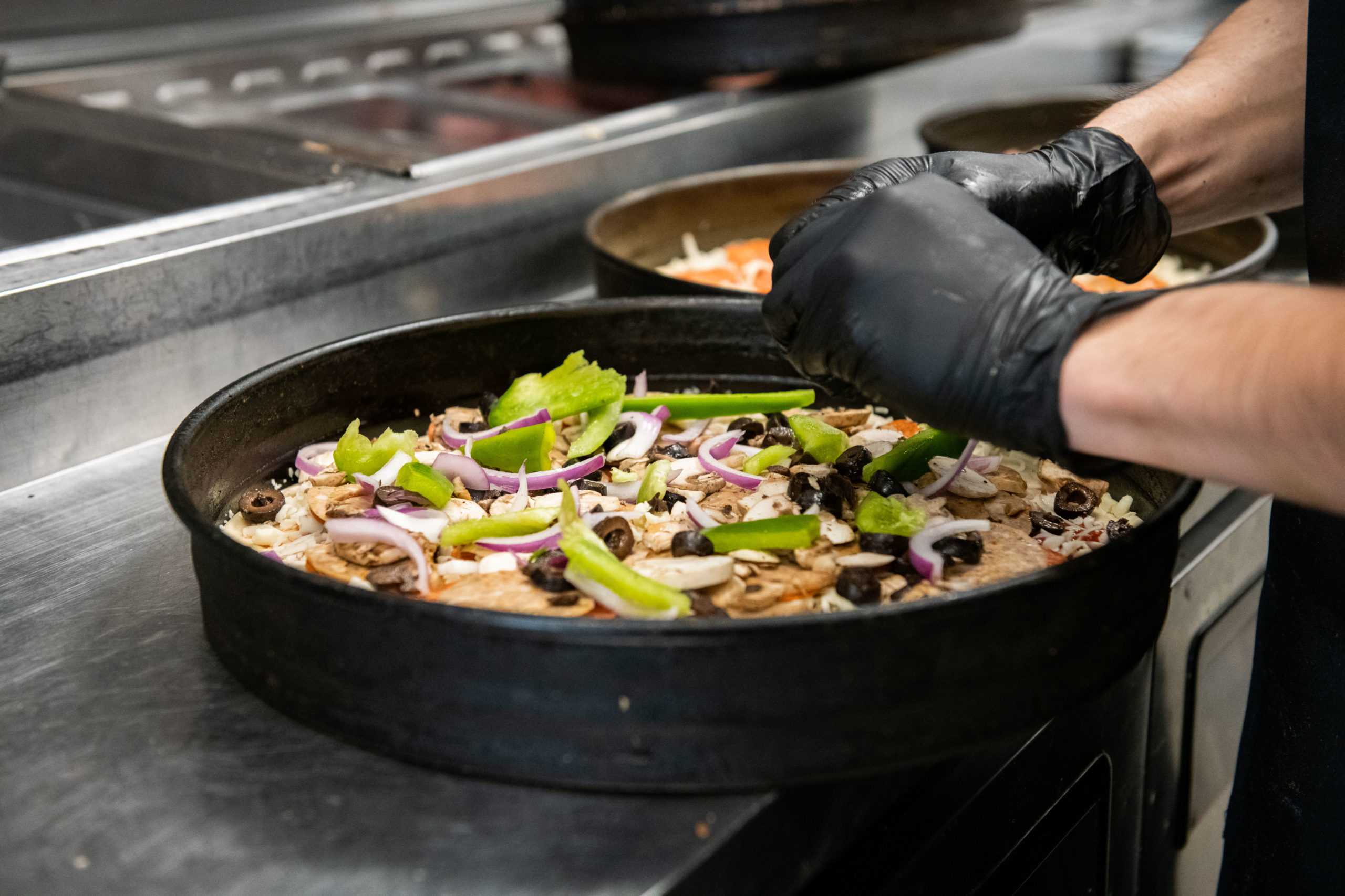 worker putting on toppings for a Krazy Karls pizza