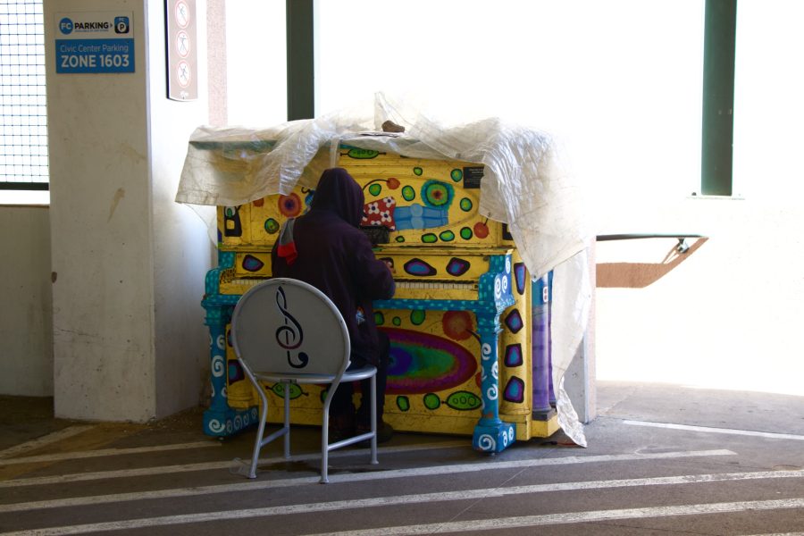 person in dark hoodie playing a brightly painted piano in a Fort Collins parking garage