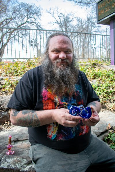 Glassblowing artist Perry (Skye) Norton smiles while holding up one of his creations outside of the Kind Creation Smoke Shop in Fort Collins March 24.